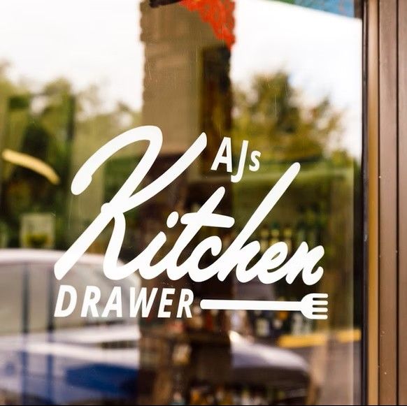 AJ's Kitchen Drawer logo lettering applied to a storefront window