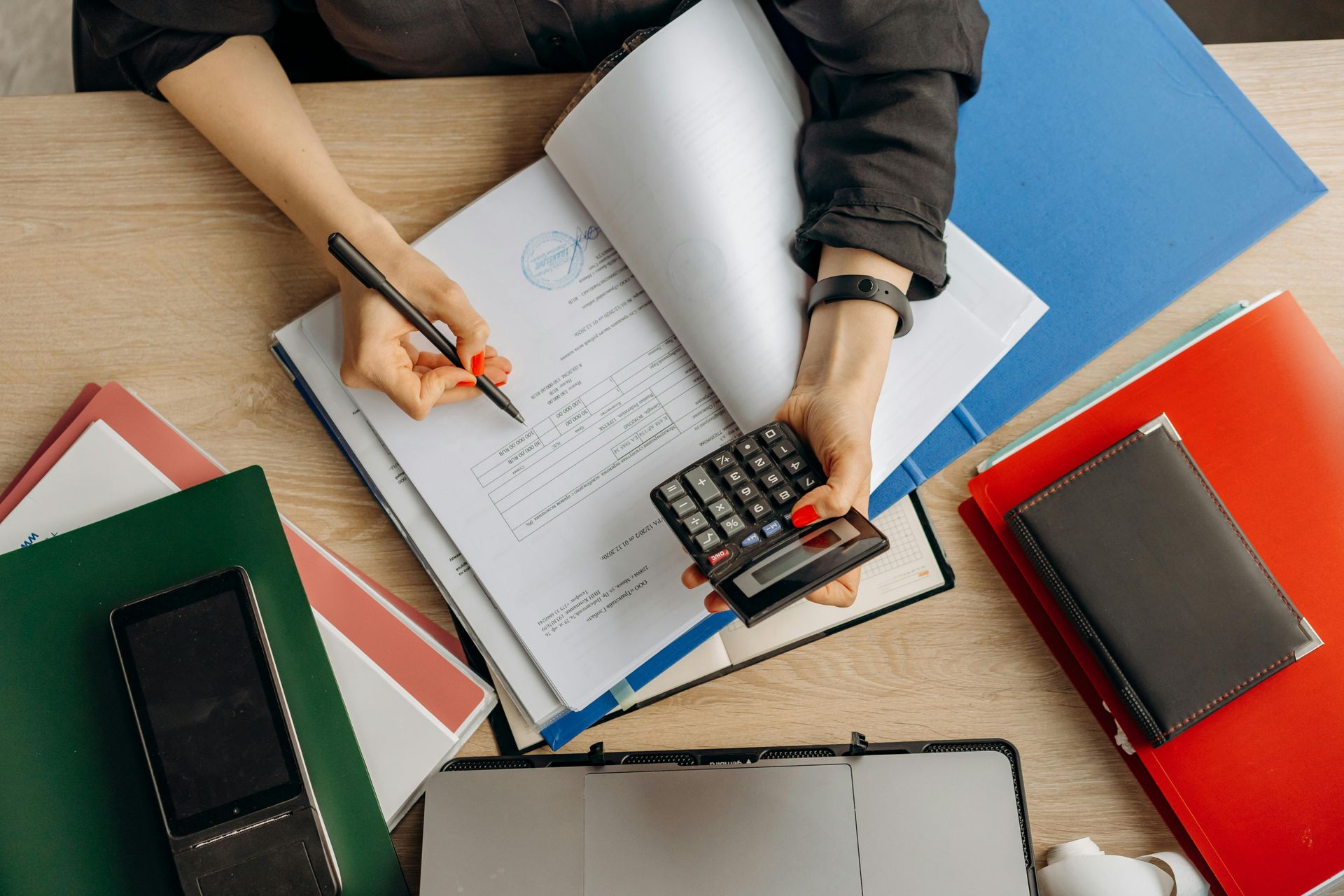 Hands with a pen reviewing financial paperwork beside an open laptop